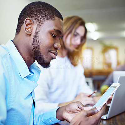 Buy stock photo Shot of a smiling young man sitting in an office using a digital tablet with a colleague in the background