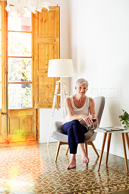 Buy stock photo Portrait of a smiling mature woman relaxing on a chair at home with a glass of wine