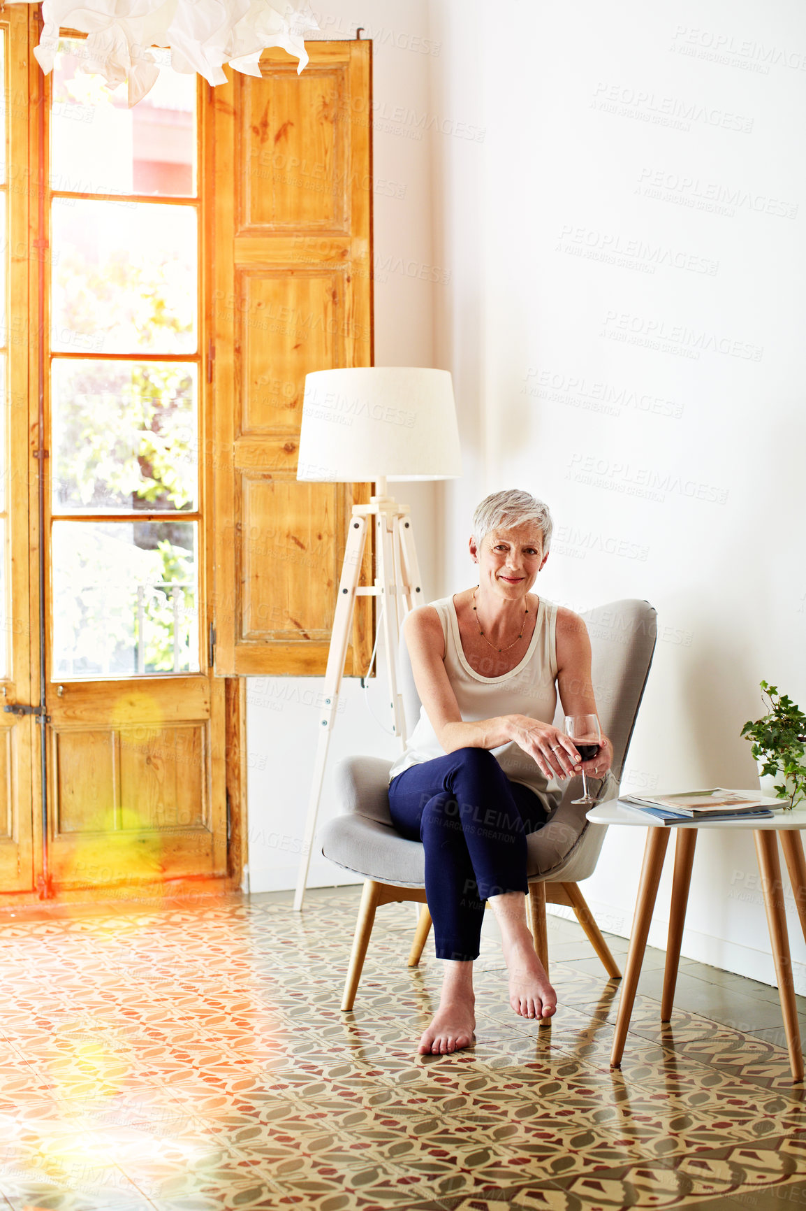 Buy stock photo Portrait of a smiling mature woman relaxing on a chair at home with a glass of wine