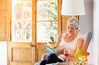 Buy stock photo Shot of a mature woman relaxing on her sofa at home reading a book