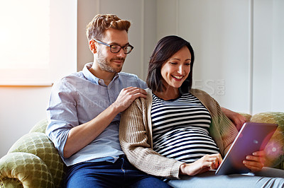 Buy stock photo Shot of a pregnant woman and her husband sitting on their sofa using a digital tablet