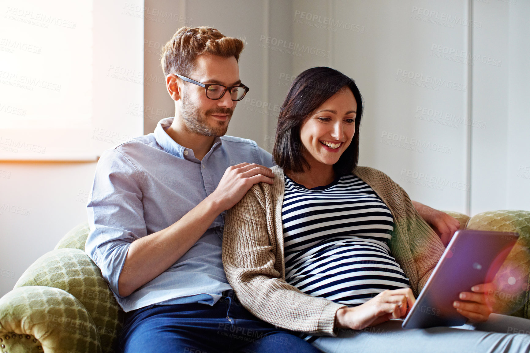 Buy stock photo Shot of a pregnant woman and her husband sitting on their sofa using a digital tablet