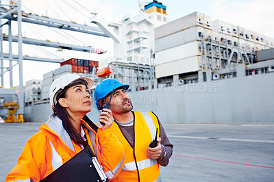 Buy stock photo Shot of two coworkers in protective workwear standing on a large commercial dock