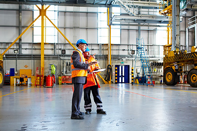 Buy stock photo Shot of two warehouse workers talking together over a clipboard inside of a large warehouse