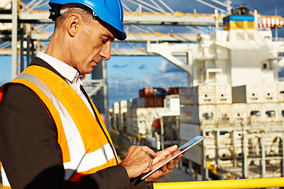 Buy stock photo Shot of a man in workwear standing on a walkway using a digital tablet over at a large commercial dock
