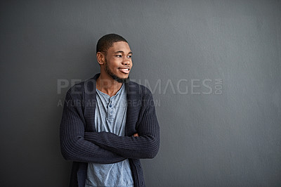 Buy stock photo Shot of a smiling young man standing with his arms crossed against a gray wall