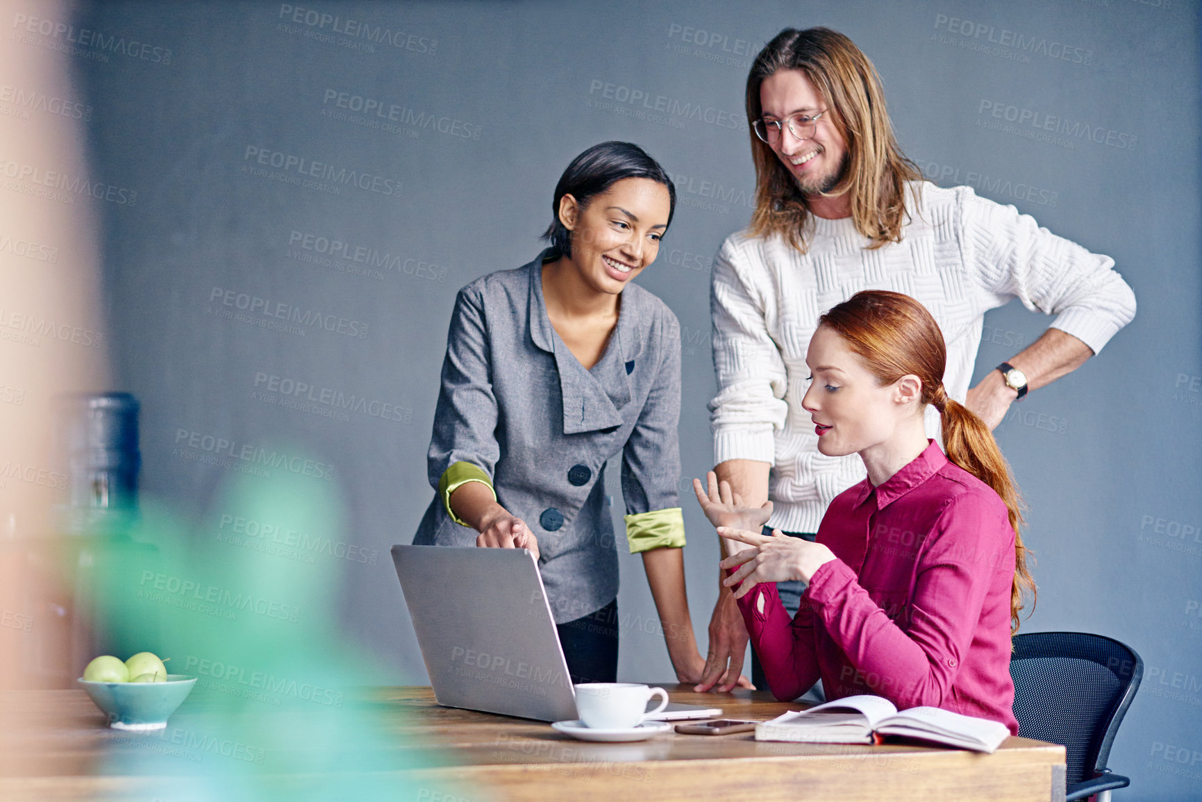 Buy stock photo Shot of a group of colleagues talking together over a laptop on a desk in an office