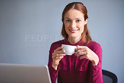 Buy stock photo Portrait of a young woman drinking a cup of coffee while working on a laptop at a desk in an office