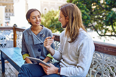 Buy stock photo Shot of two young designers sitting together on a bench outside of their office using a digital tablet