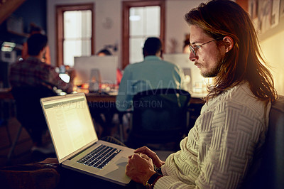 Buy stock photo Shot of a young designer working on a laptop in an office late in the evening