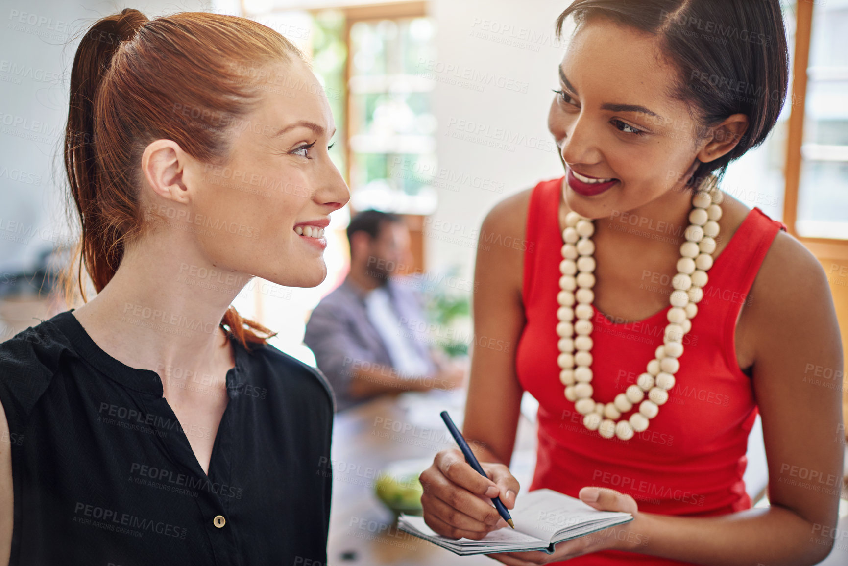 Buy stock photo Shot of two young colleagues talking together while working in an office