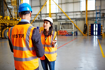 Buy stock photo Shot of two dock workers talking together inside of a large warehouse