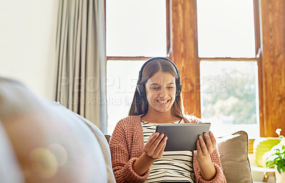 Buy stock photo Shot of a smiling young woman sitting on her sofa watching a movie on a digital tablet with headphones