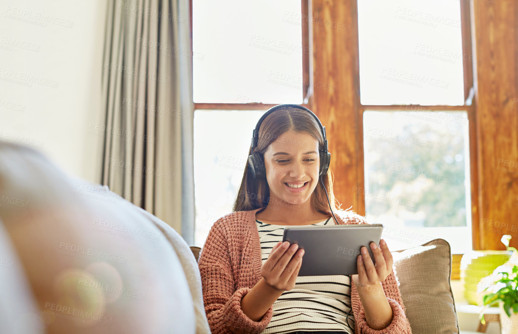Buy stock photo Shot of a smiling young woman sitting on her sofa watching a movie on a digital tablet with headphones