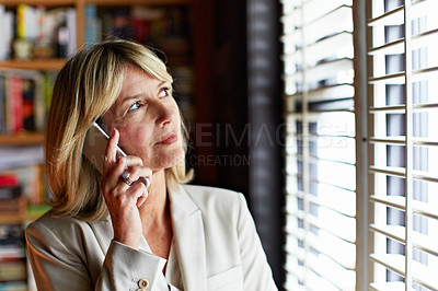 Buy stock photo Shot of a mature businesswoman looking out the window while talking on her cellphone