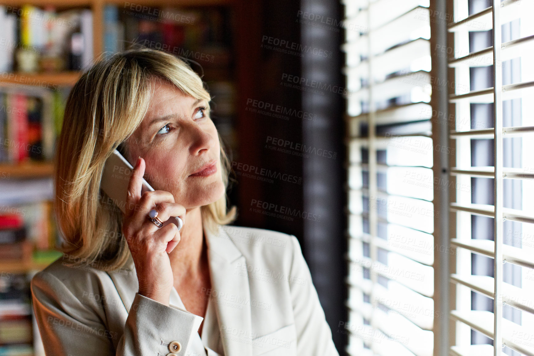 Buy stock photo Shot of a mature businesswoman looking out the window while talking on her cellphone