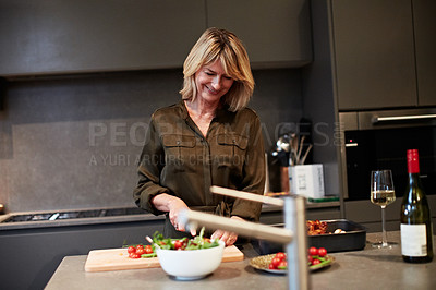 Buy stock photo Shot of a mature woman enjoying a glass of wine while preparing dinner in the kitchen