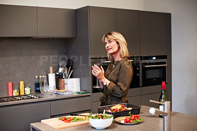 Buy stock photo Shot of a mature woman enjoying a glass of wine while preparing dinner in the kitchen