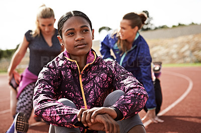 Buy stock photo Shot of a young woman sitting on the track with fellow athletes sitting in the background