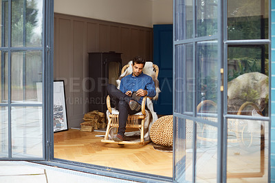 Buy stock photo Shot of a young man using a digital tablet while relaxing on a rocking chair at home