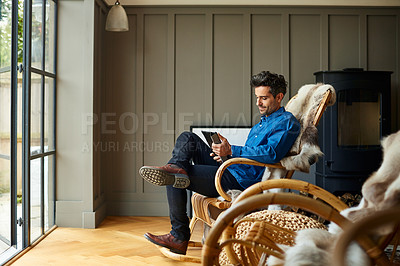 Buy stock photo Shot of a young man using a digital tablet while relaxing on a rocking chair at home
