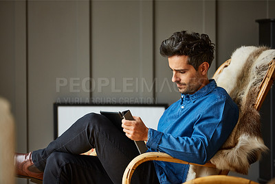 Buy stock photo Shot of a young man using a digital tablet while relaxing on a rocking chair at home