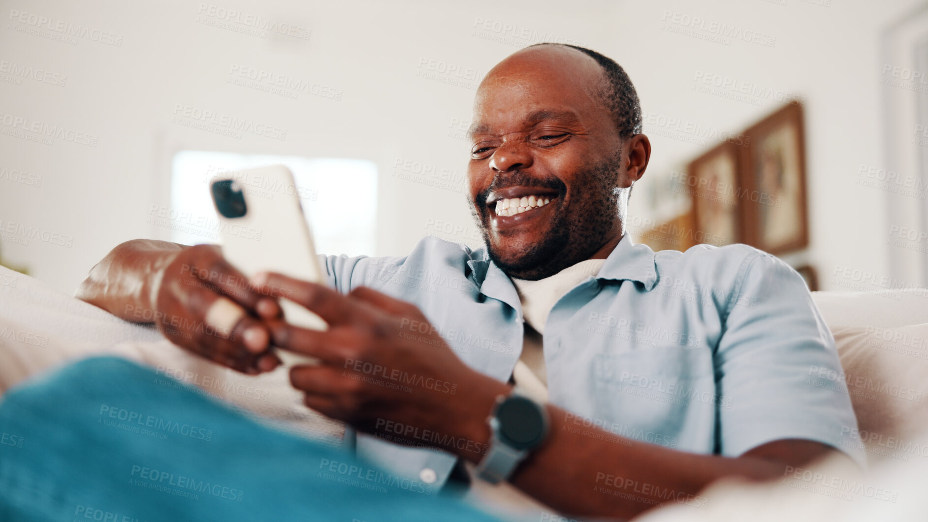 Buy stock photo Text, phone and black man in home with laugh, online communication and comic post on social media. Happy, digital and mature person on sofa with tech, funny message or meme reaction on chat app.