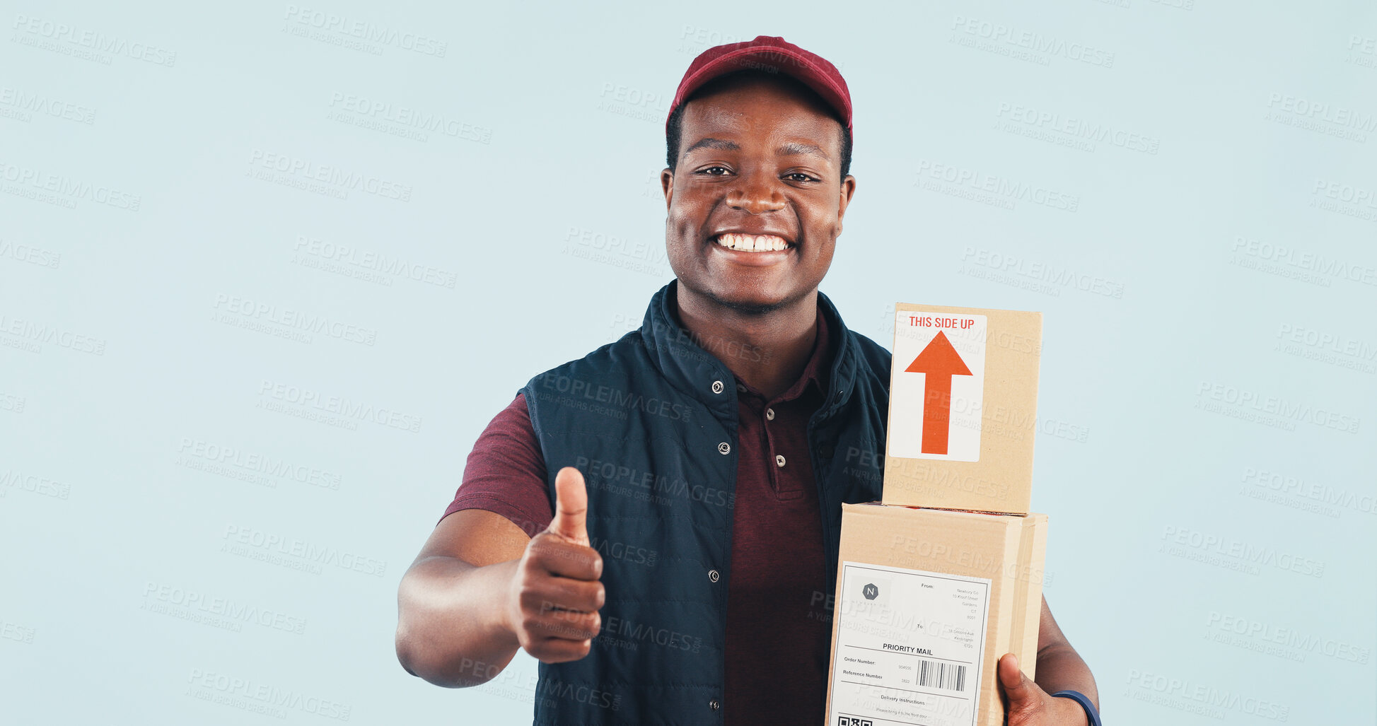 Buy stock photo Portrait, boxes and delivery man in studio with thumbs up, postal service and online shopping package. Happy, black person and courier with ecommerce order, like emoji and space on blue background.