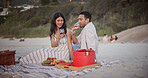 Love, picnic or couple at beach with wine glass, holiday together or bonding on anniversary celebration. Happy, fruit or people with alcohol, partner connection or special moment on outdoor honeymoon