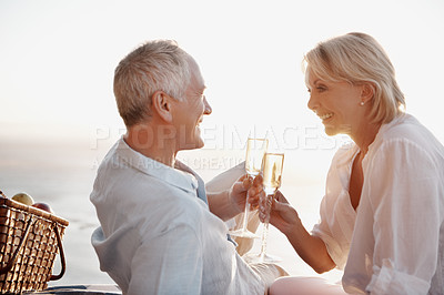 Buy stock photo Couple, smile and cheers at ocean with champagne, celebrate milestone and picnic with love. Mature people, happiness and toast with drink for bonding, relationship appreciation and outing at beach