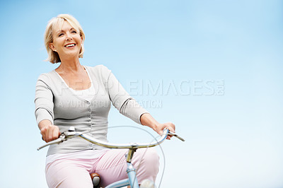 Buy stock photo Sky, cycling and senior woman on bicycle, mockup space and commute with eco friendly bike or travel. Outdoor, low angle and mature person on trip, happiness and transport with zero carbon emissions