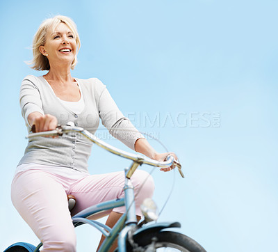 Buy stock photo Sky, travel and senior woman on bicycle, mockup space and commute with eco friendly bike or cycling. Outdoor, low angle and mature person on trip, happiness and transport with zero carbon emissions