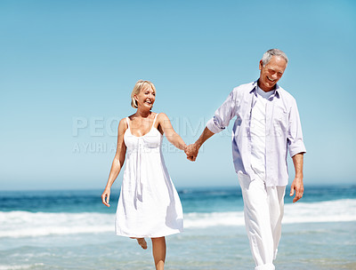 Buy stock photo Couple, smile and holding hands at ocean with love, walking or commitment for anniversary. Space, happy and mature people at beach with affection, marriage milestone or healthy relationship with care