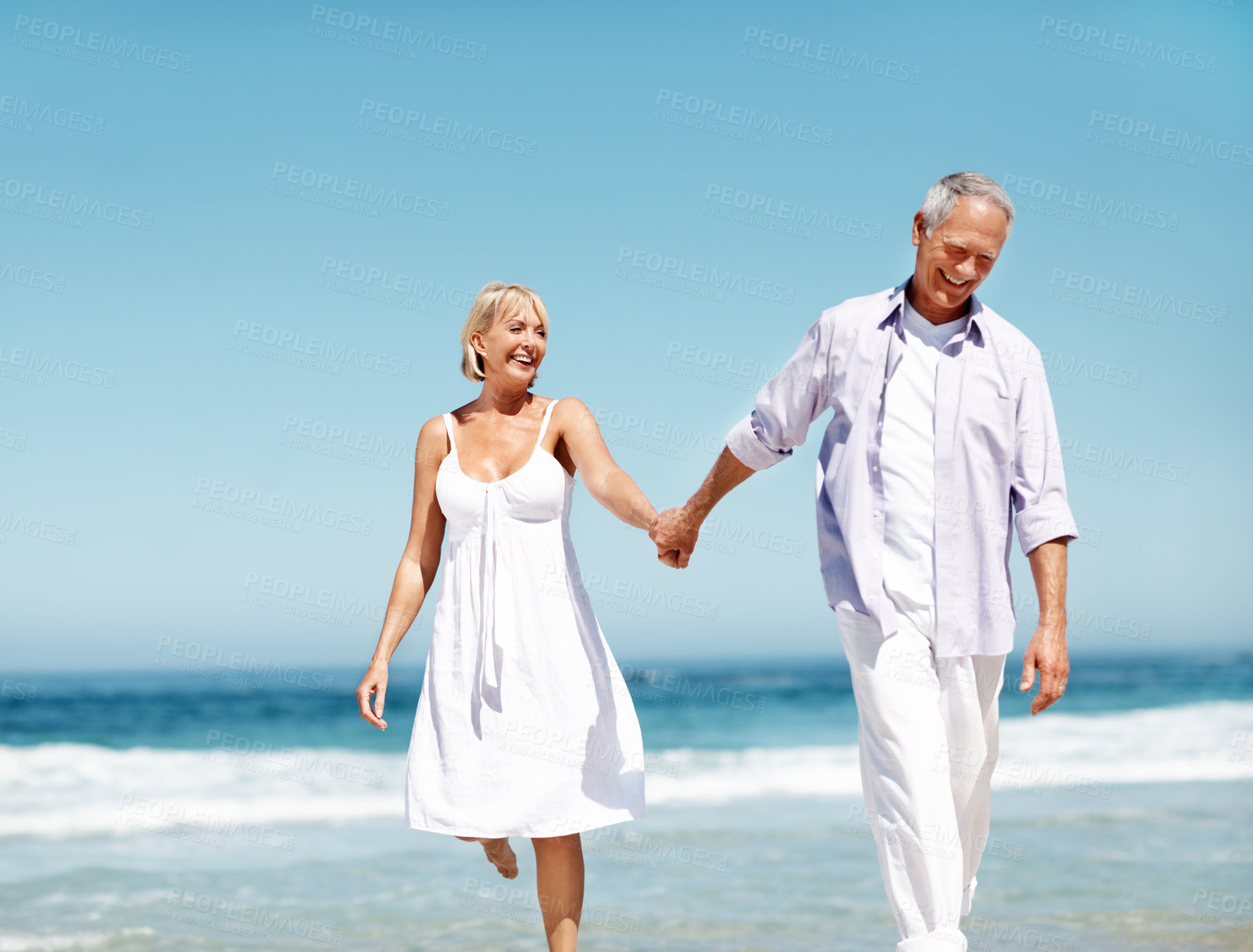 Buy stock photo Couple, smile and holding hands at ocean with love, walking or commitment for anniversary. Space, happy and mature people at beach with affection, marriage milestone or healthy relationship with care