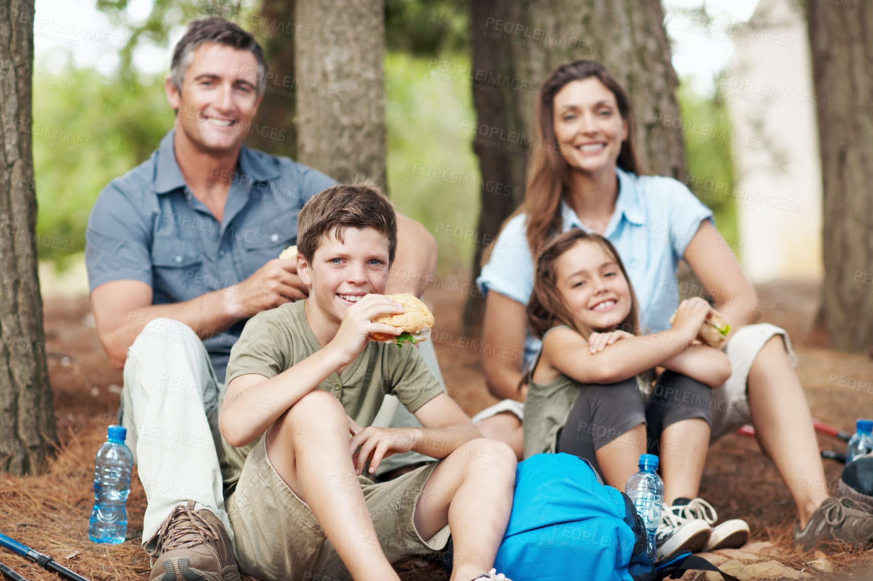 Buy stock photo Hiking, children and parents eating on break in forest for nutrition, burger meal and holiday travel. Trekking, people and happy kids with food in portrait for hunger, lunch or bonding on family trip