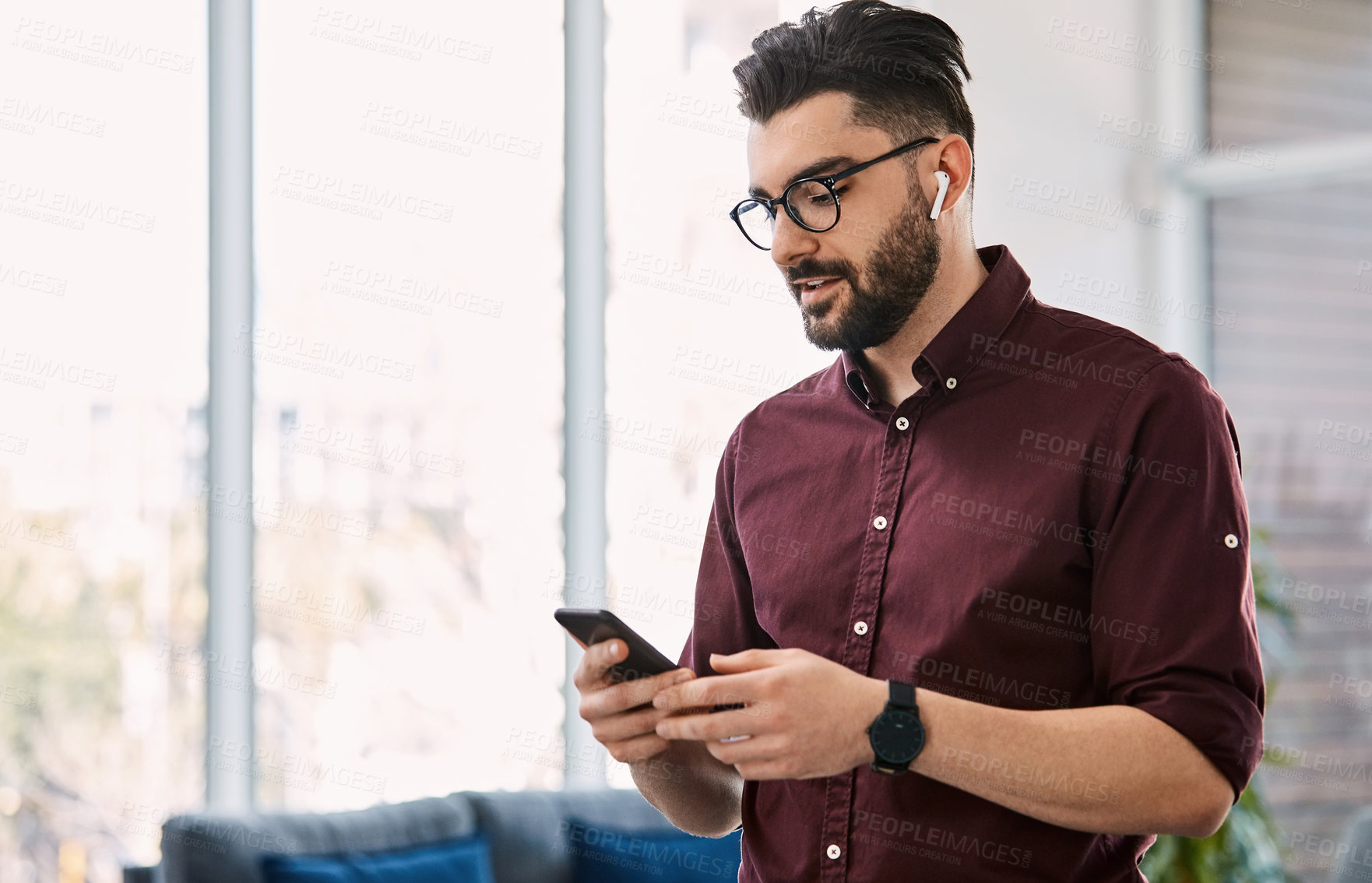 Buy stock photo Shot of a handsome young businessman using a cellphone in his office at work