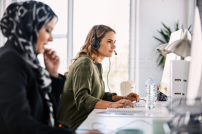 Buy stock photo Shot of a group of young call centre agents wearing headsets and working on their computers in an office