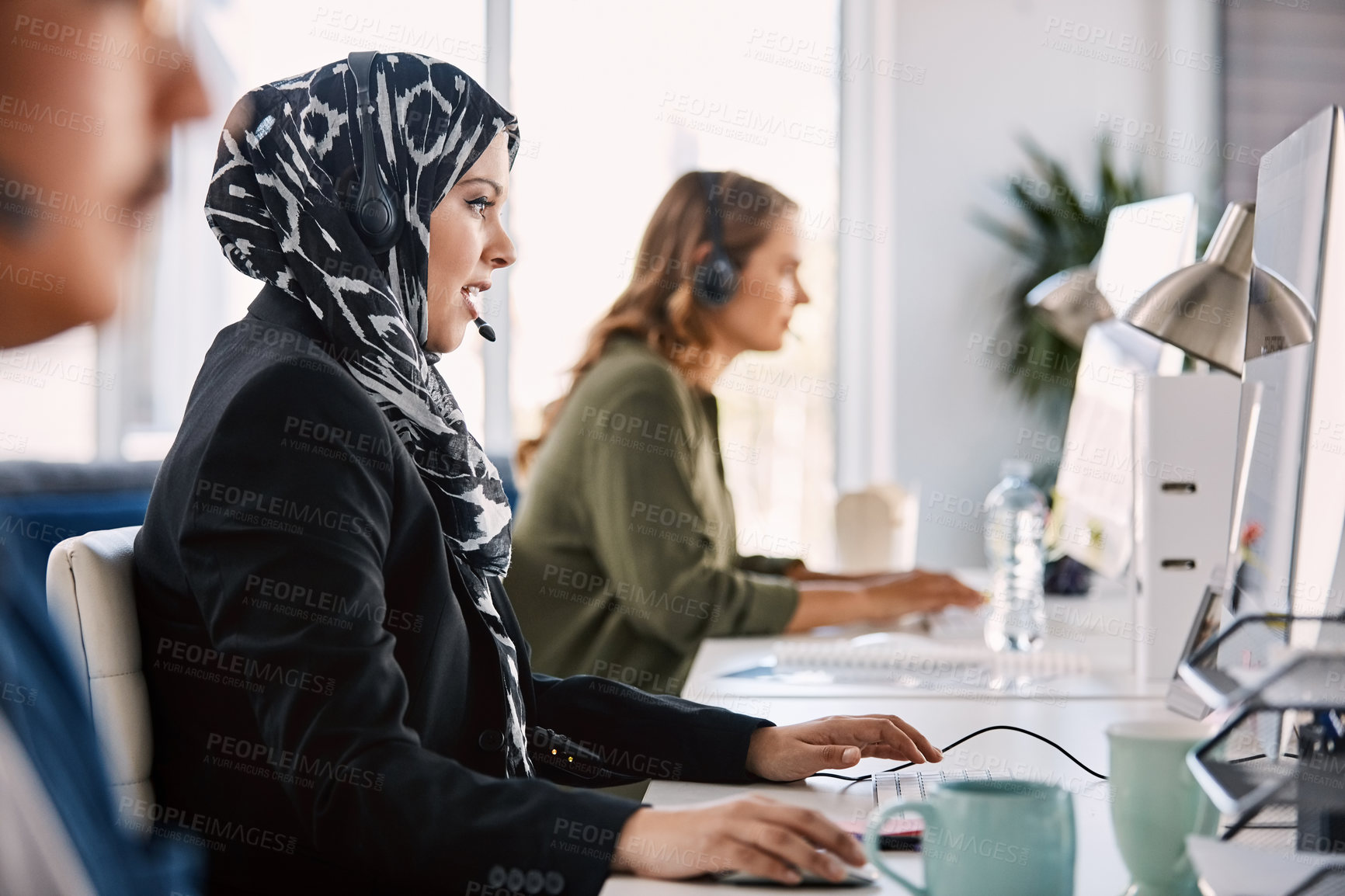 Buy stock photo Shot of a group of young call centre agents wearing headsets and working on their computers in an office