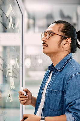 Buy stock photo Shot of a handsome young businessman planning and writing notes on a glass wall in his office