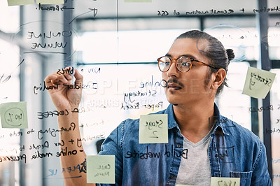 Buy stock photo Shot of a handsome young businessman planning and writing notes on a glass wall in his office