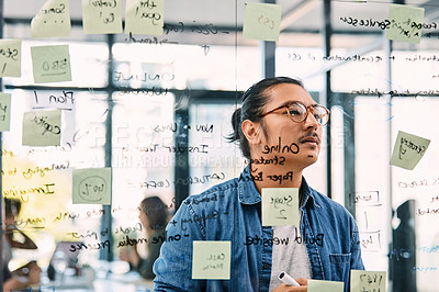 Buy stock photo Shot of a handsome young businessman planning and writing notes on a glass wall in his office