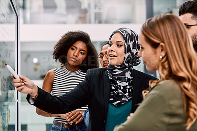 Buy stock photo Shot of a group of young businesspeople planning and writing notes on a glass wall in an office at work
