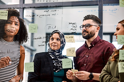 Buy stock photo Shot of a group of young businesspeople planning and writing notes on a glass wall in an office at work