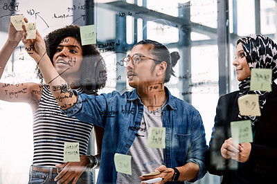 Buy stock photo Shot of a group of young businesspeople planning and writing notes on a glass wall in an office at work