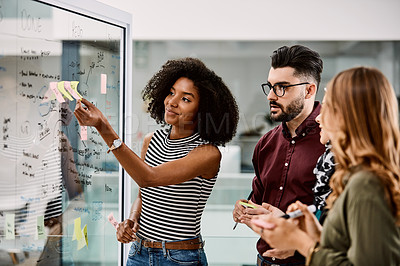 Buy stock photo Shot of a group of young businesspeople planning and writing notes on a glass wall in an office at work