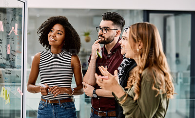 Buy stock photo Shot of a group of young businesspeople planning and writing notes on a glass wall in an office at work