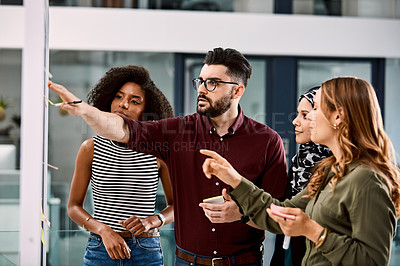 Buy stock photo Shot of a group of young businesspeople planning and writing notes on a glass wall in an office at work