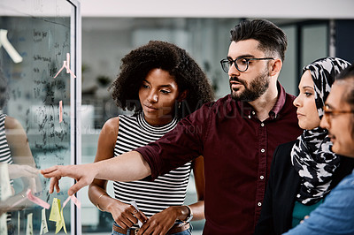 Buy stock photo Shot of a group of young businesspeople planning and writing notes on a glass wall in an office at work