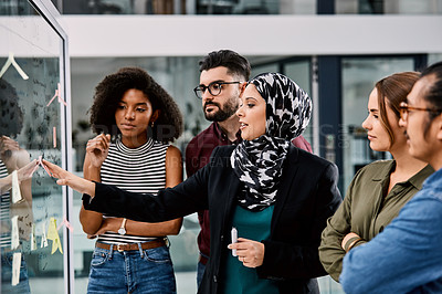 Buy stock photo Shot of a group of young businesspeople planning and writing notes on a glass wall in an office at work