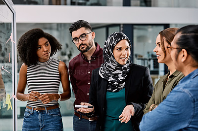 Buy stock photo Shot of a group of young businesspeople planning and writing notes on a glass wall in an office at work